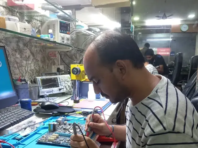Technician probing a computer motherboard with a multimeter and soldering iron