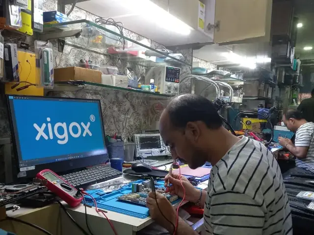 Technician probing a computer motherboard with a multimeter and soldering iron