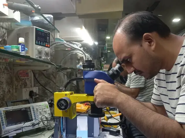 Technician inspecting a laptop motherboard under a microscope at the repair bench