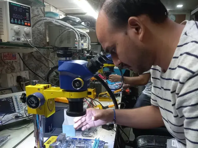 Technician inspecting a laptop motherboard under a microscope at the repair bench
