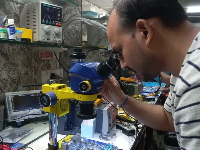 Technician inspecting a laptop motherboard under a microscope at the repair bench