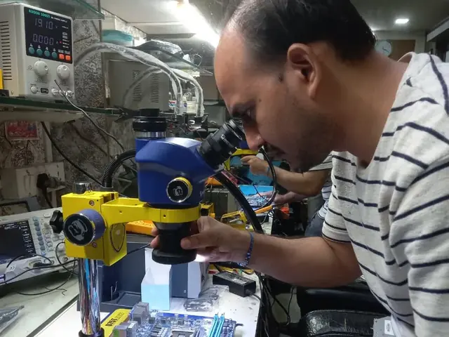 Technician inspecting a laptop motherboard under a microscope at the repair bench