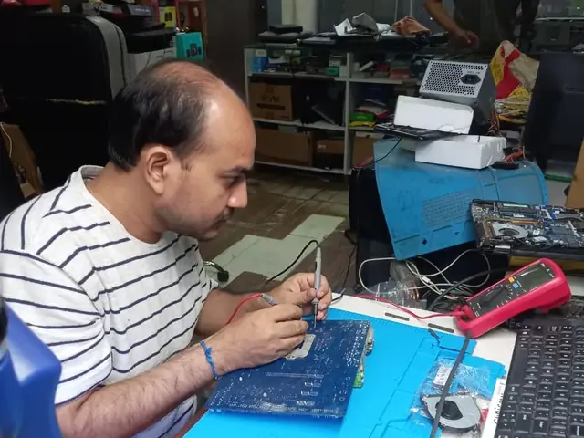 Technician probing a computer motherboard with a multimeter and soldering iron
