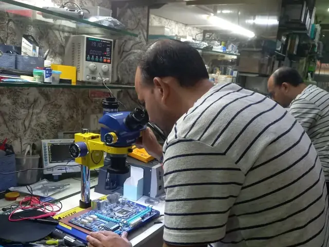 Technician inspecting a laptop motherboard under a microscope at the repair bench