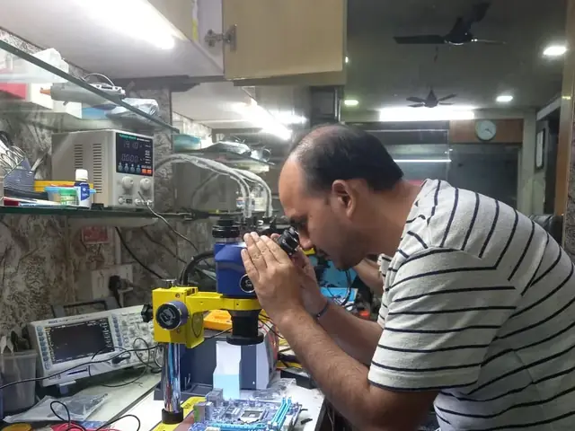 Technician inspecting a laptop motherboard under a microscope at the repair bench