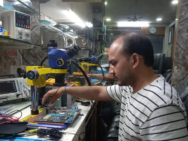 Technician inspecting a laptop motherboard under a microscope at the repair bench