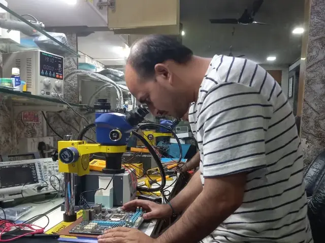Technician inspecting a laptop motherboard under a microscope at the repair bench