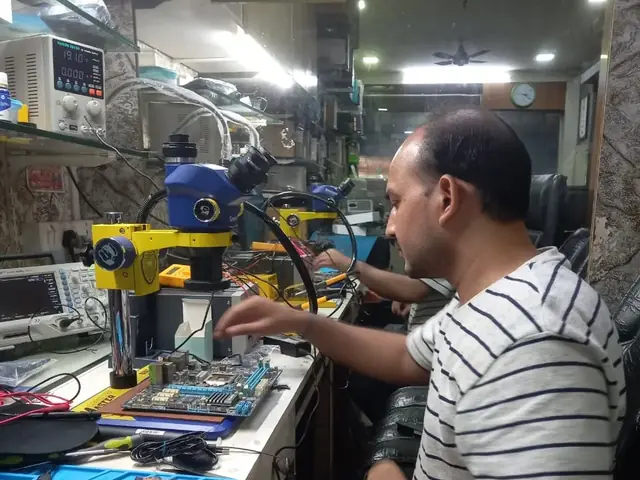 Technician inspecting a laptop motherboard under a microscope at the repair bench