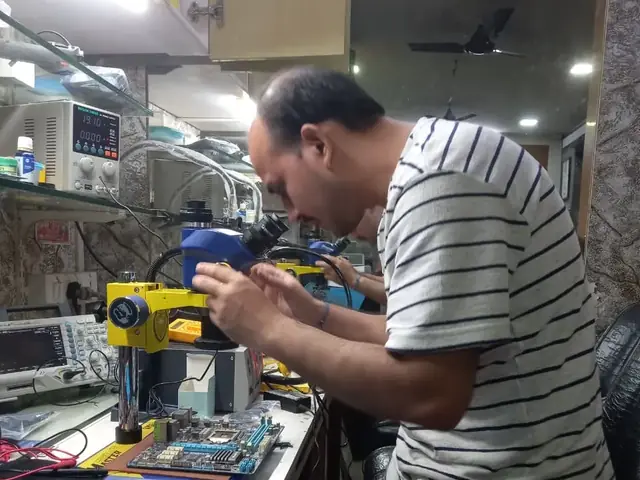 Technician inspecting a laptop motherboard under a microscope at the repair bench