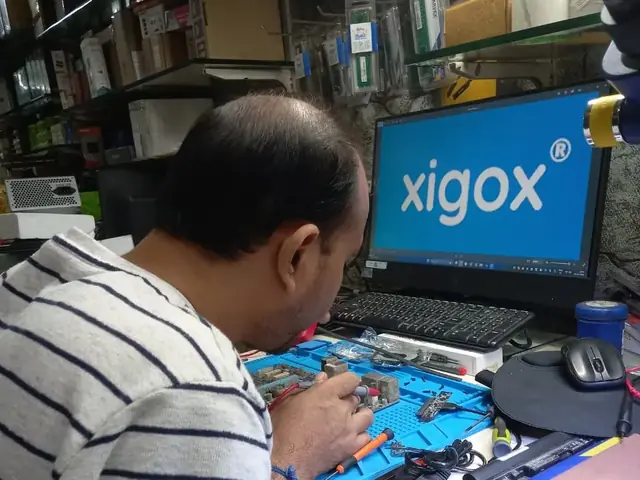 Technician probing a computer motherboard with a multimeter and soldering iron