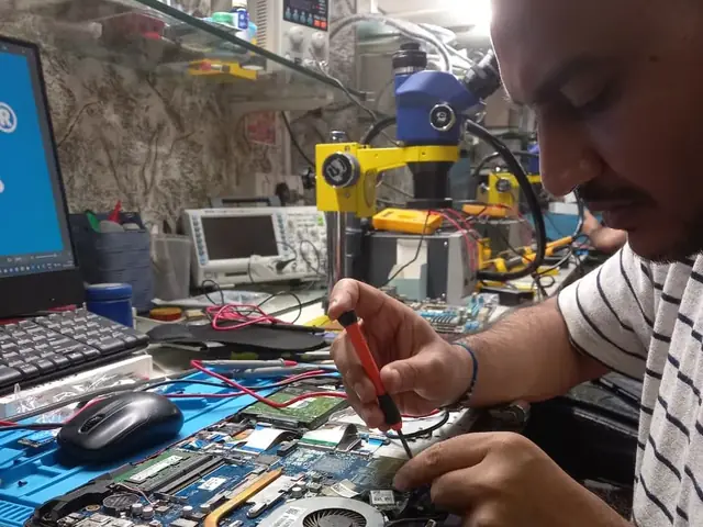 Technician testing a laptop mainboard with a multimeter beside a Xigox-branded monitor