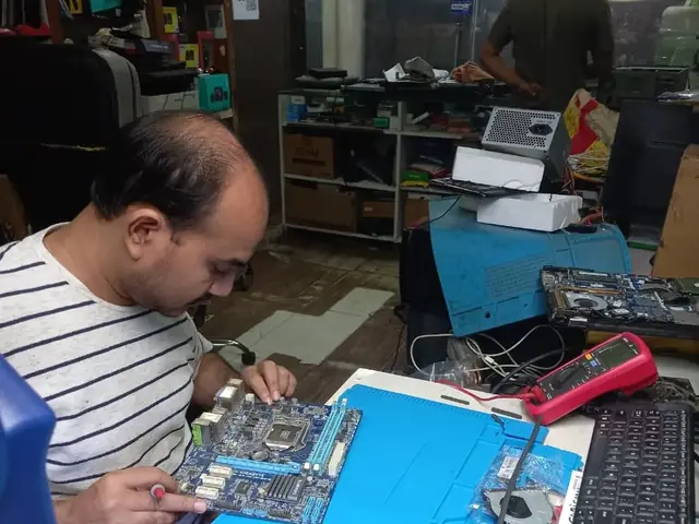 Technician probing a computer motherboard with a multimeter and soldering iron