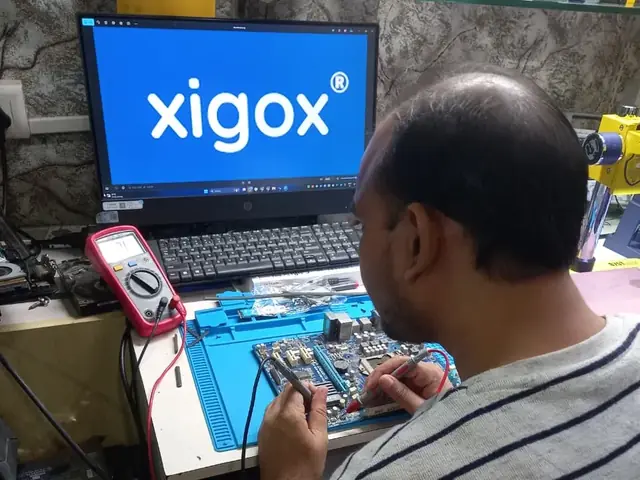 Technician probing a computer motherboard with a multimeter and soldering iron
