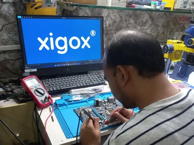 Technician probing a computer motherboard with a multimeter and soldering iron