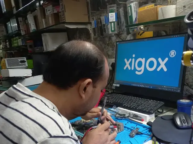 Technician probing a computer motherboard with a multimeter and soldering iron
