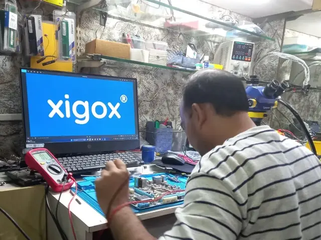 Technician probing a computer motherboard with a multimeter and soldering iron