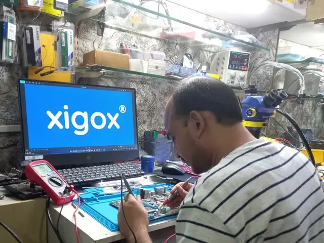 Technician probing a computer motherboard with a multimeter and soldering iron
