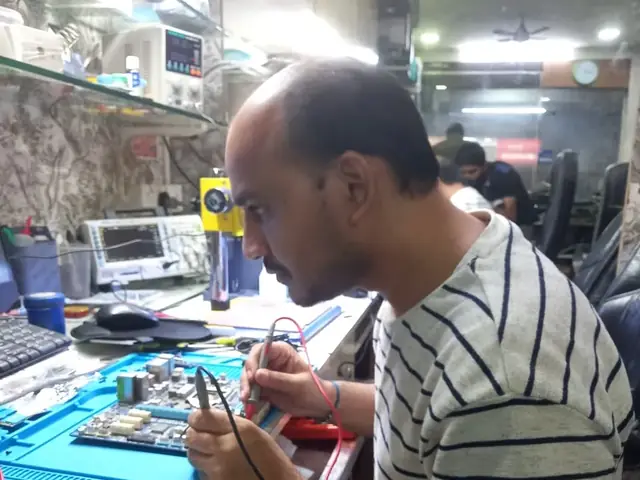 Technician probing a computer motherboard with a multimeter and soldering iron