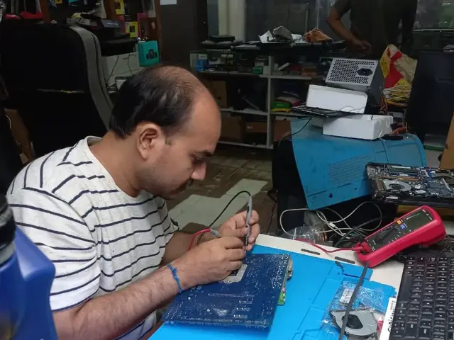 Technician probing a computer motherboard with a multimeter and soldering iron