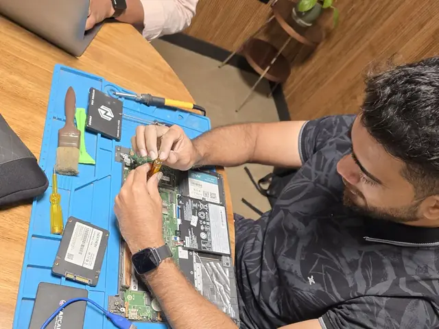 Opened laptop on an anti-static mat with SSDs, a cleaning brush and pry tools laid out