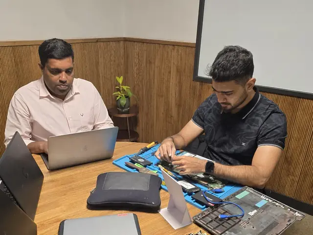 Two Xigox technicians at a table, one working on an opened laptop on a repair mat