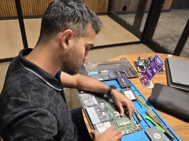 Technician working on an opened laptop motherboard on an anti-static mat with an SSD beside it