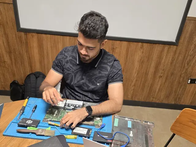 Technician working on an opened laptop motherboard on an anti-static mat with an SSD beside it