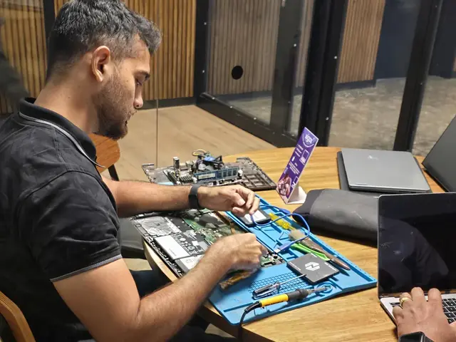 Technician repairing an opened laptop with an SSD and repair tools laid out on the mat
