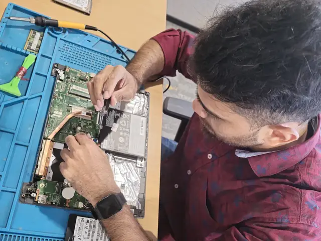 Technician working inside an opened laptop with RAM modules and an SSD laid out beside it