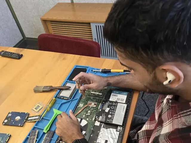 Technician with a screwdriver over an opened laptop, RAM modules and hard drives on the repair mat