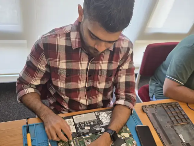 Technician with a screwdriver over an opened laptop, RAM modules and hard drives on the repair mat