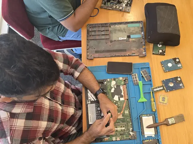 Technician with a screwdriver over an opened laptop, RAM modules and hard drives on the repair mat