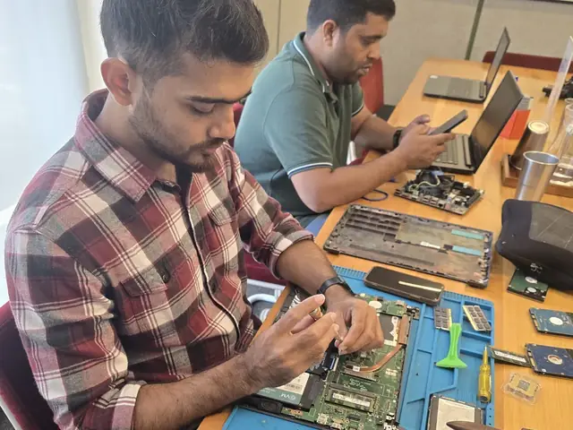 Technician working on a laptop with hard drives, RAM modules and a cleaning brush on the mat