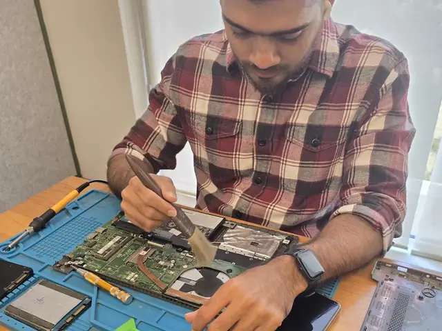 Technician brushing dust off an opened laptop motherboard with a cleaning brush