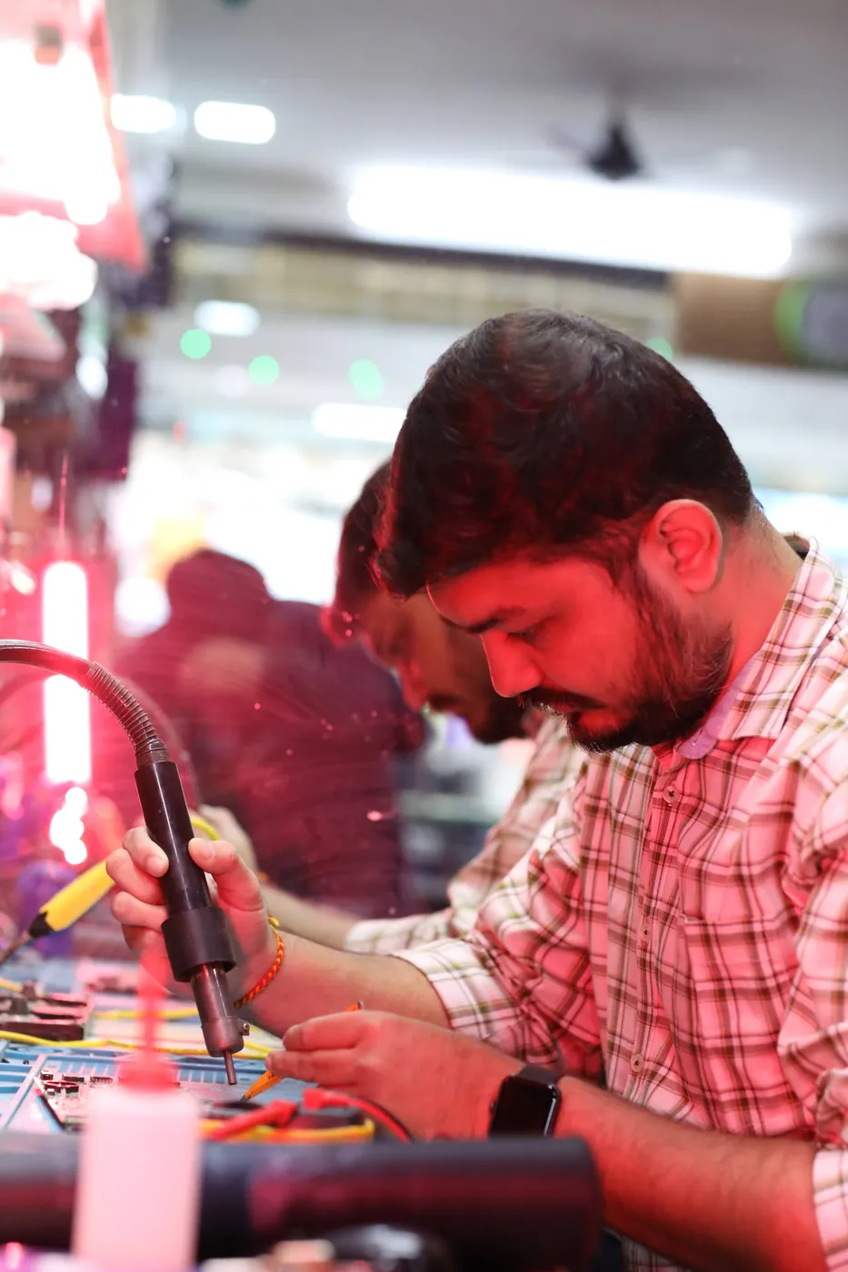Technician soldering on a laptop board with a fume-extractor arm and a multimeter on the bench