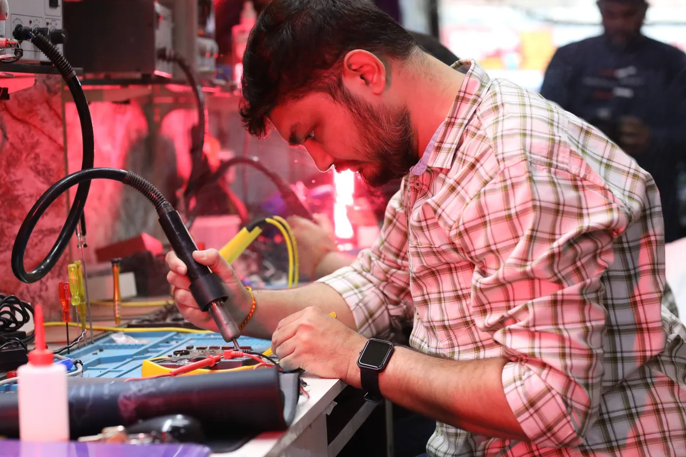 Technician soldering on a laptop board with a fume-extractor arm and a multimeter on the bench
