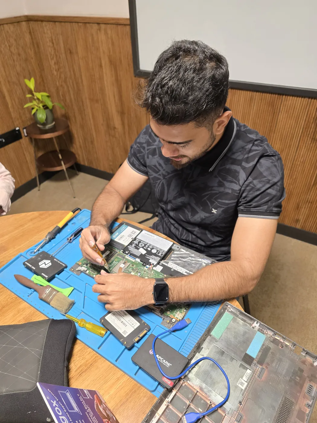 Technician working on an opened laptop with SSDs and tools laid out on an anti-static repair mat