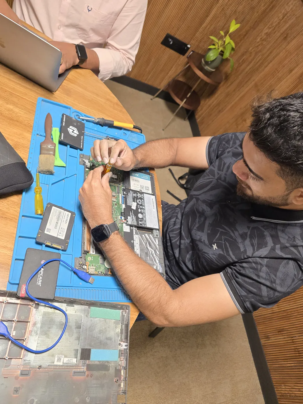 Opened laptop on an anti-static mat with SSDs, a cleaning brush and pry tools laid out