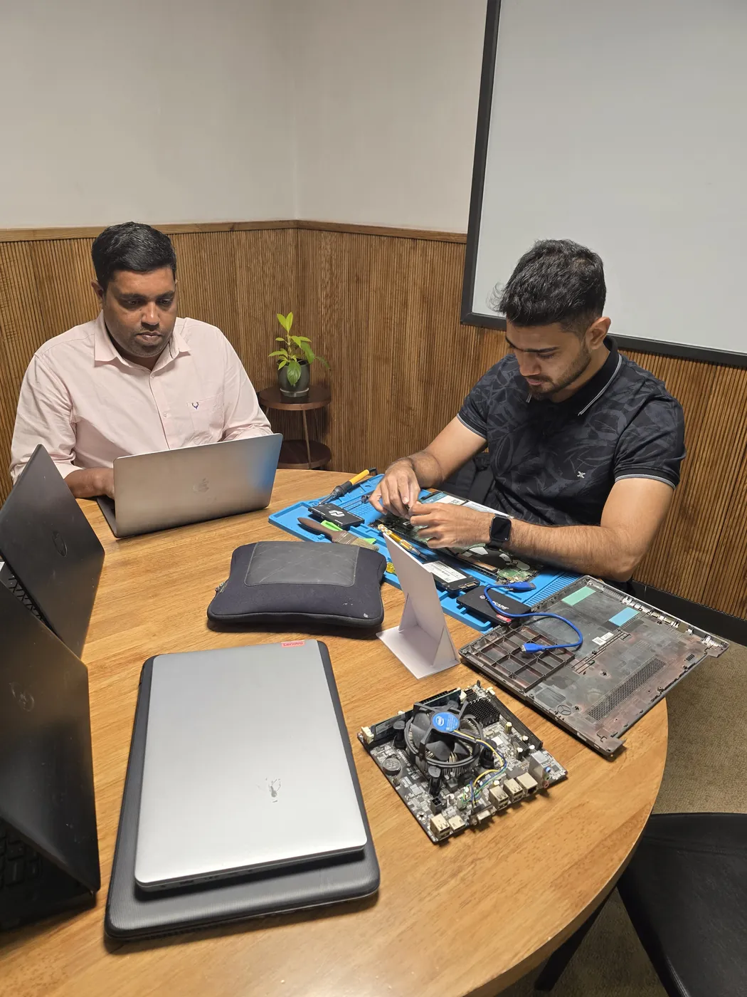 Two Xigox technicians at a table, one working on an opened laptop on a repair mat