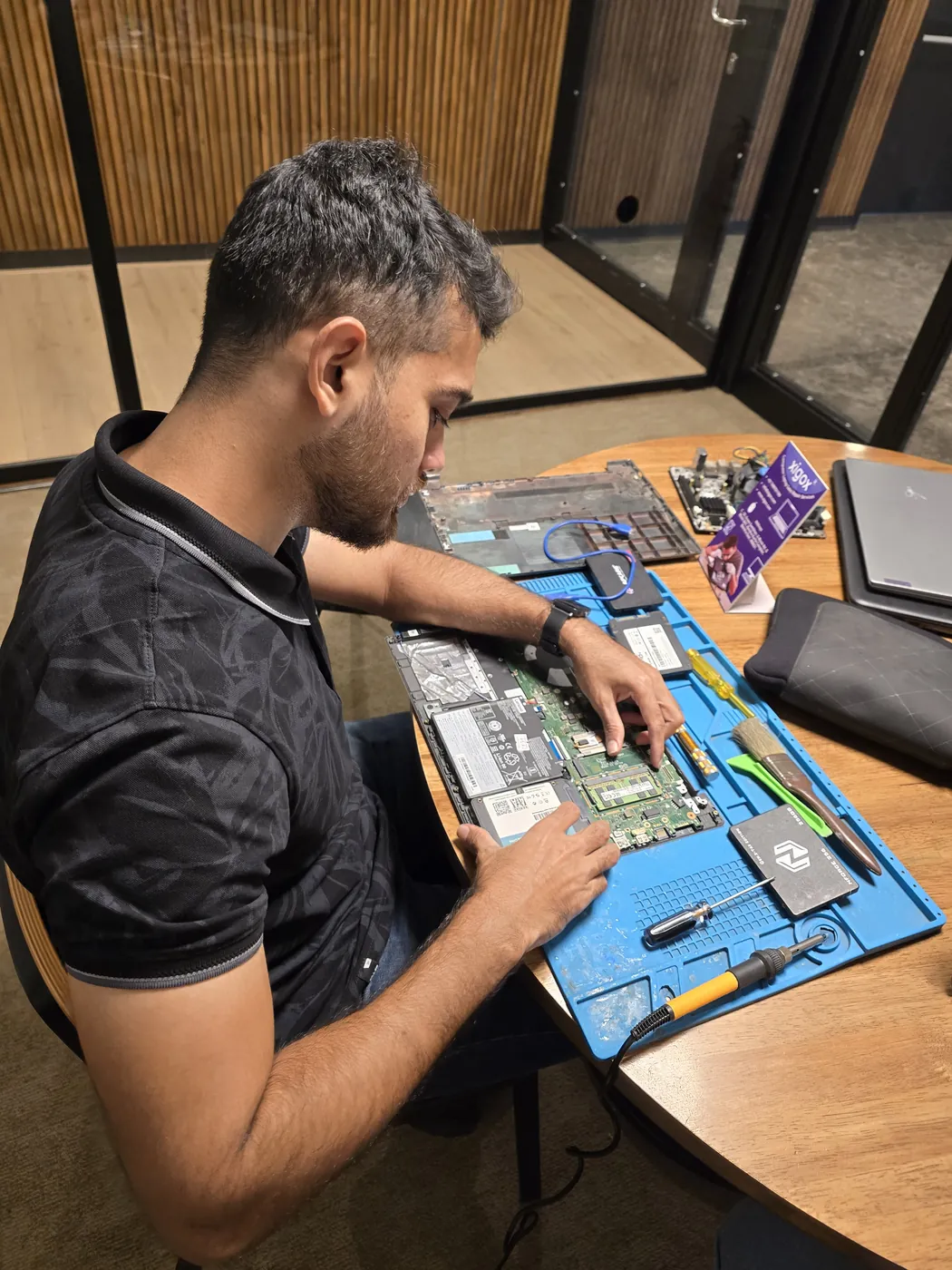 Technician working on an opened laptop motherboard on an anti-static mat with an SSD beside it