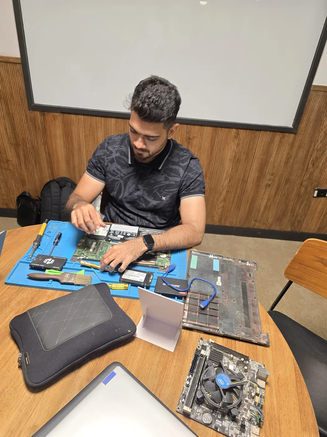 Technician working on an opened laptop motherboard on an anti-static mat with an SSD beside it