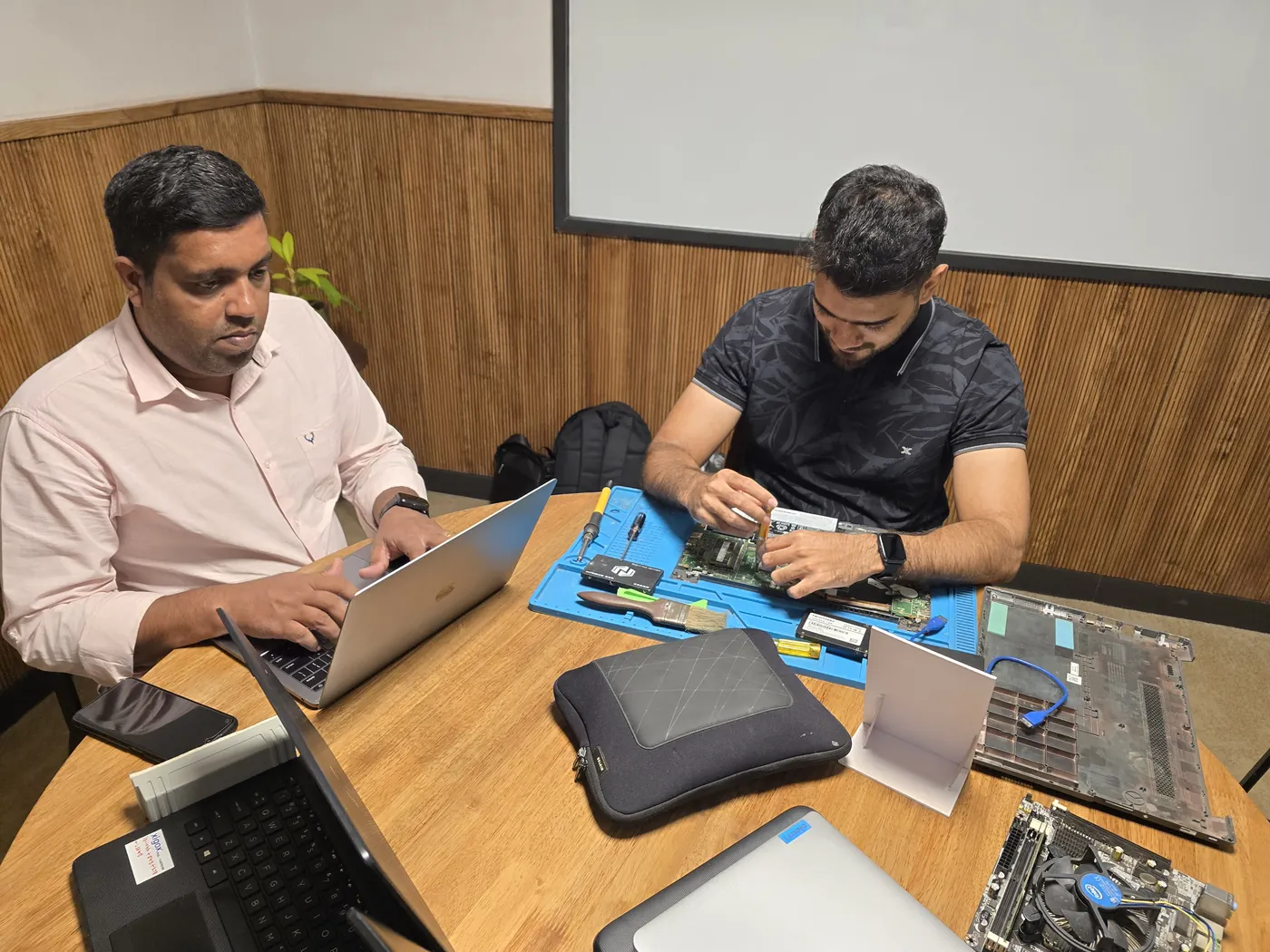 Two technicians at work, one repairing an opened laptop on an anti-static mat