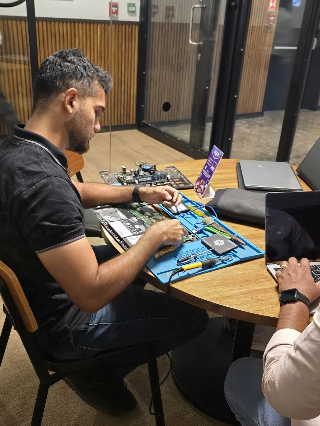 Technician repairing an opened laptop with an SSD and repair tools laid out on the mat