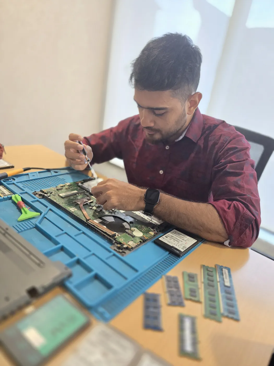 Technician working inside an opened laptop with RAM modules and an SSD laid out beside it
