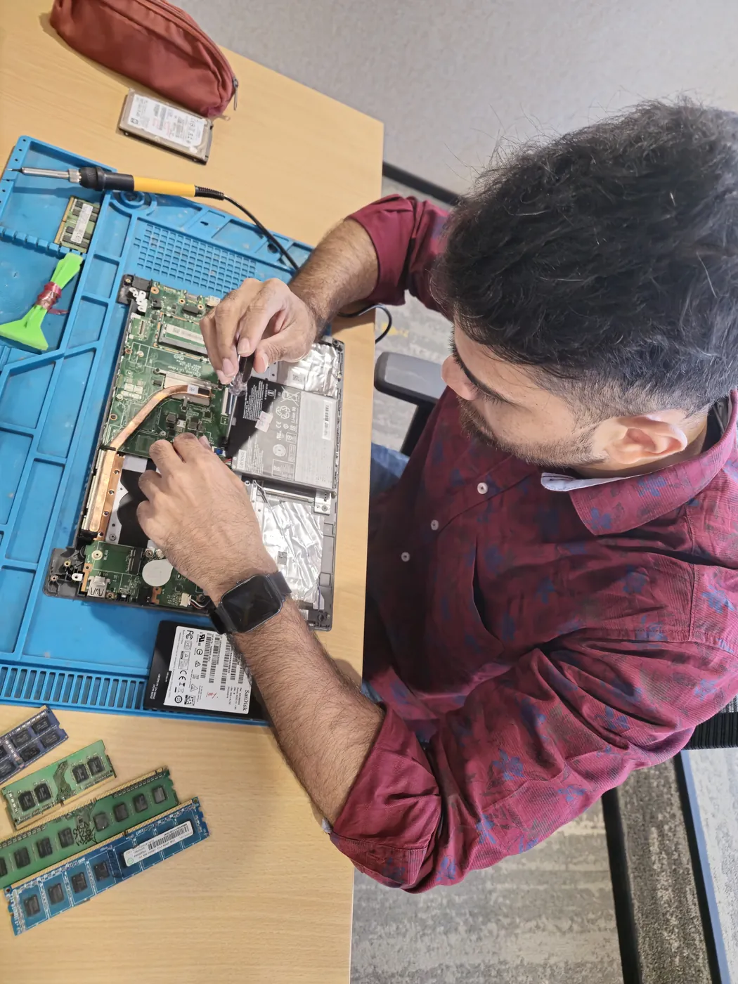 Technician working inside an opened laptop with RAM modules and an SSD laid out beside it