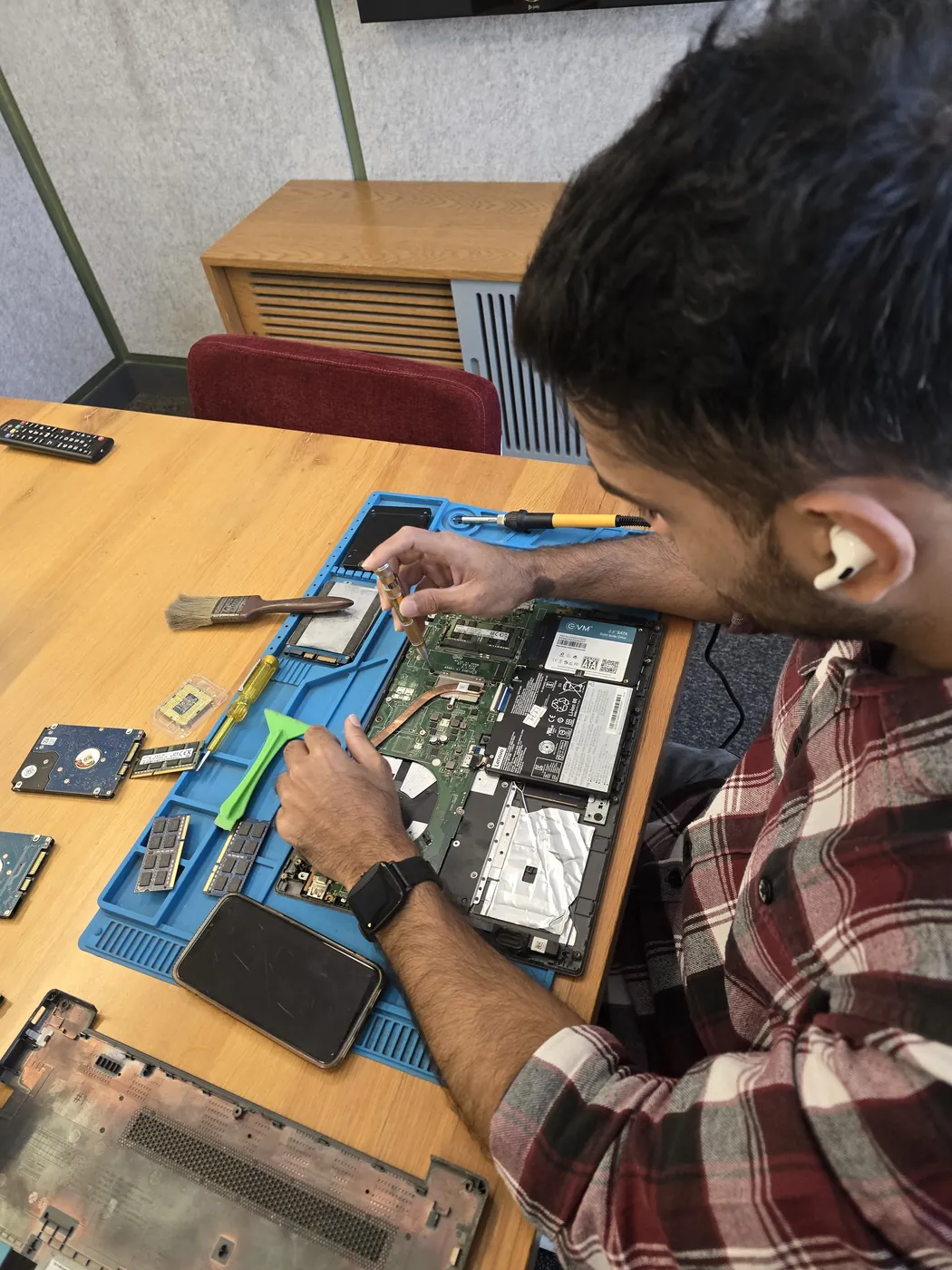 Technician with a screwdriver over an opened laptop, RAM modules and hard drives on the repair mat