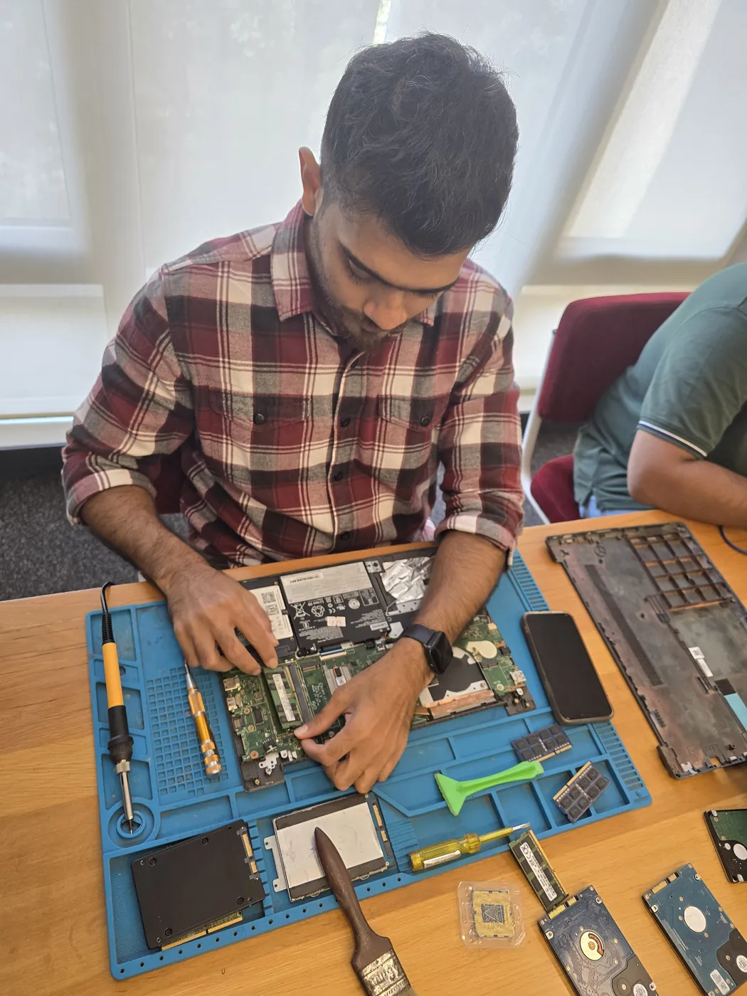 Technician with a screwdriver over an opened laptop, RAM modules and hard drives on the repair mat