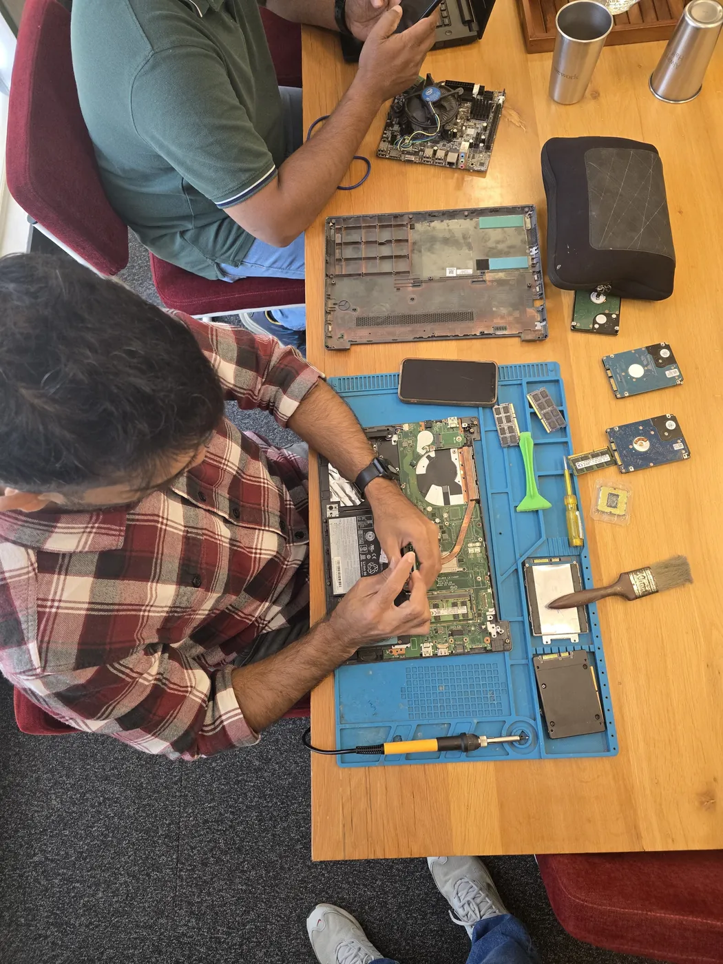 Technician with a screwdriver over an opened laptop, RAM modules and hard drives on the repair mat