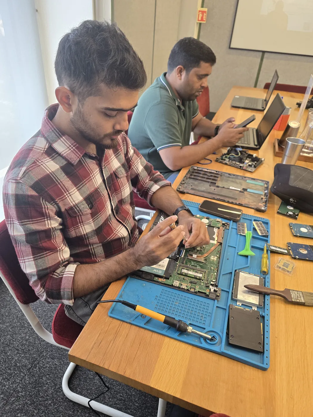 Technician working on a laptop with hard drives, RAM modules and a cleaning brush on the mat
