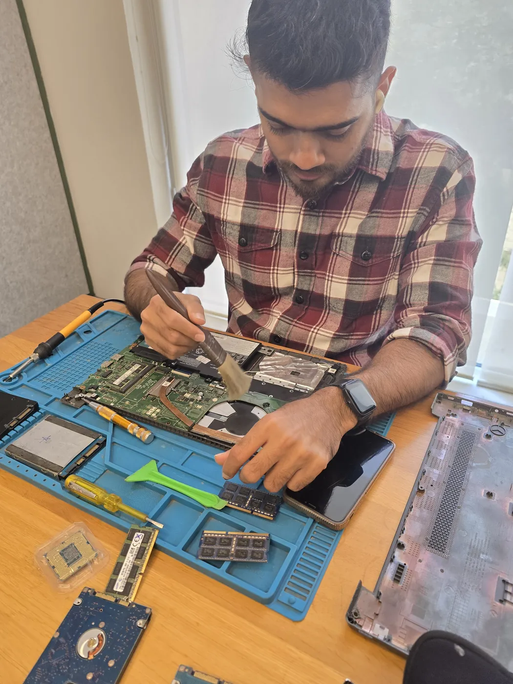 Technician brushing dust off an opened laptop motherboard with a cleaning brush